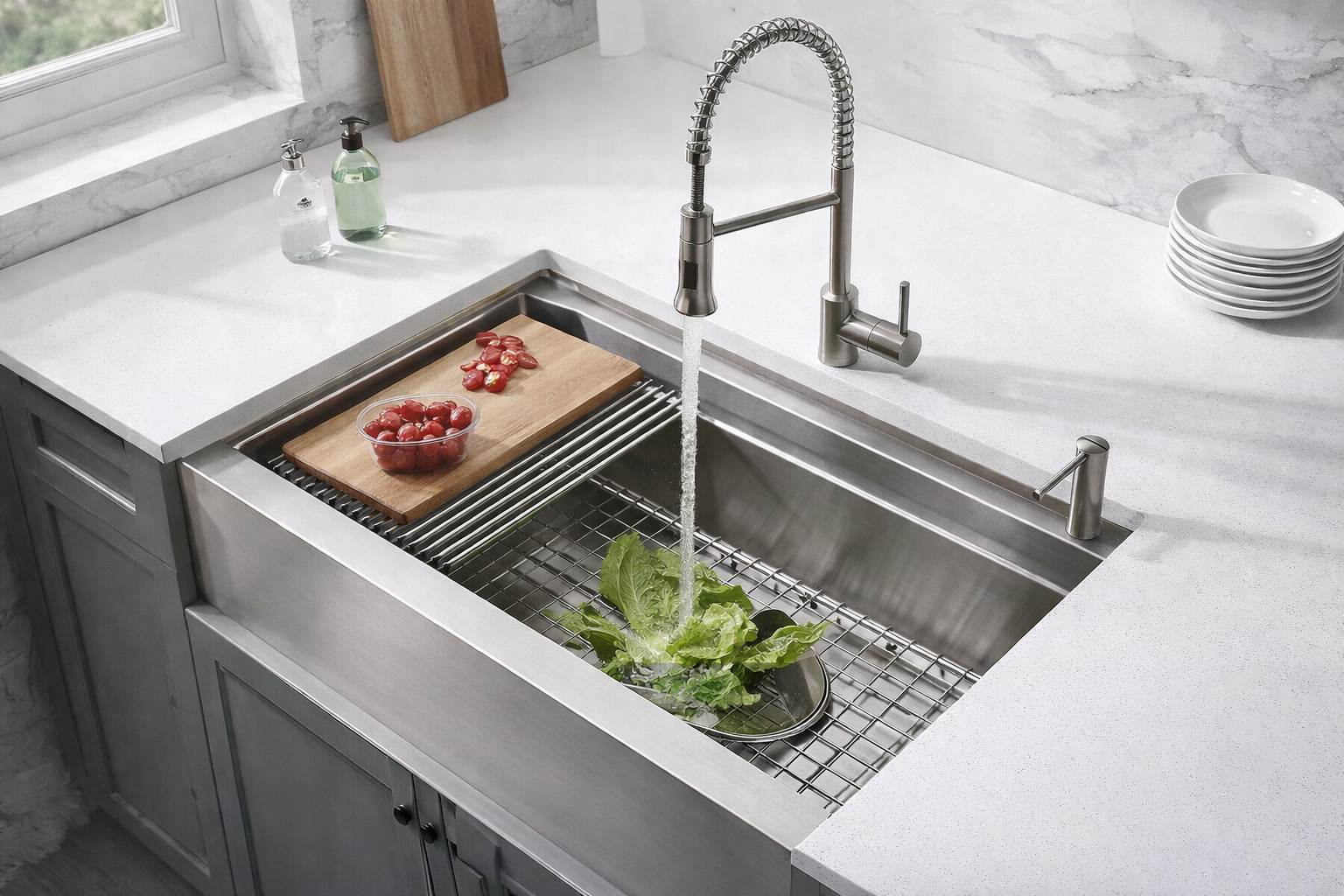 Modern stainless steel workstation kitchen sink with high-arc pull-down faucet installed in a white quartz countertop with fresh produce being rinsed.